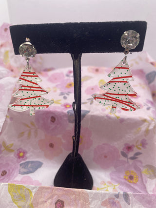 A pair of handmade white acrylic dangle earrings designed to resemble Christmas trees, displayed on a earring stand against a floral background.