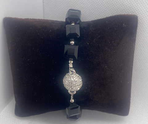 Bracelet with black beads and a silver clasp on a black cushion against a white background