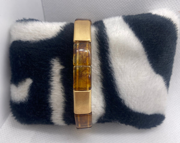 Black and white striped pillow with a gold and amber bracelet on a white background