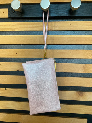 A pink shimmer wristlet crossbody purse with three compartments hanging on a hook, against a wooden background.