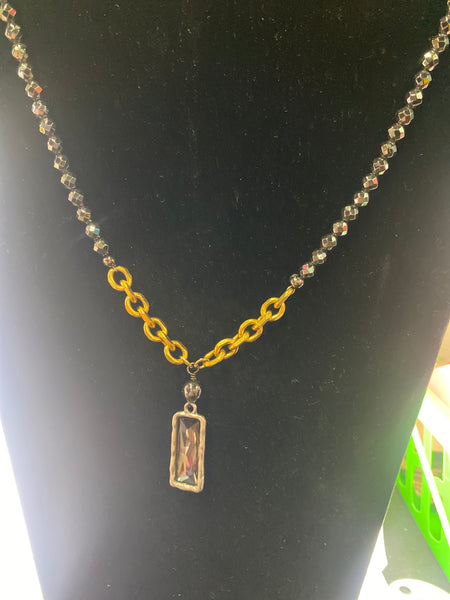 Gold chain with a rectangular pendant on a black background