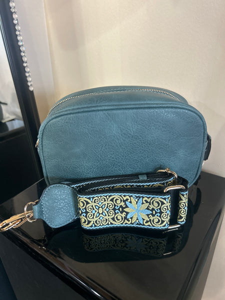 Blue textured handbag with a decorative strap on a reflective surface