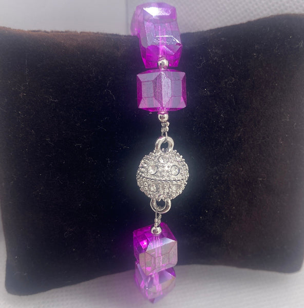 Bracelet with purple and clear beads on a black cushion against a white background