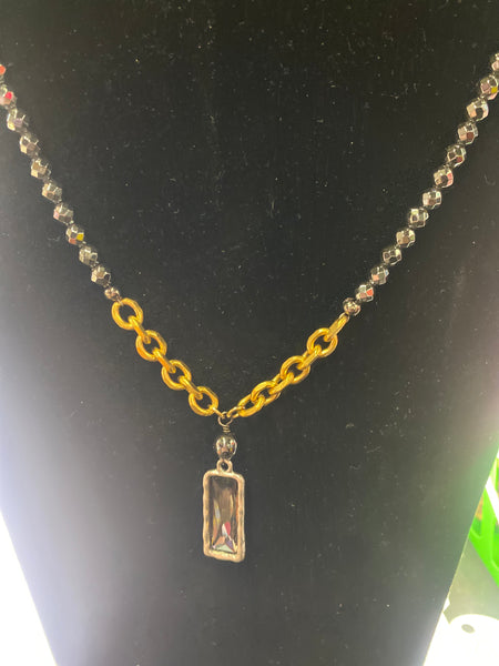 Gold chain with a rectangular pendant on a black surface
