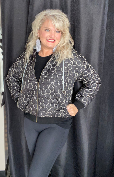 Woman wearing a patterned jacket and dark pants against a black background