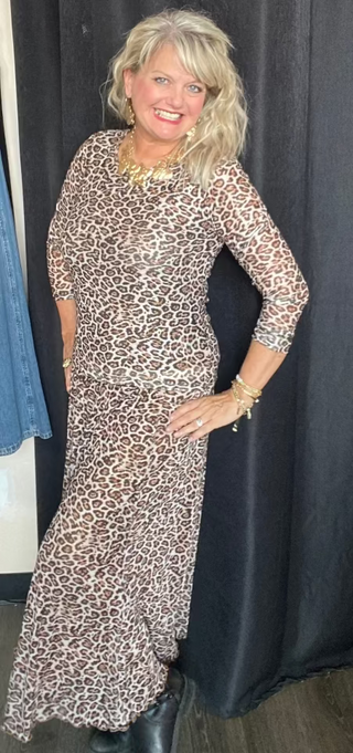 Woman wearing a leopard print skirt posing in front of a black curtain.