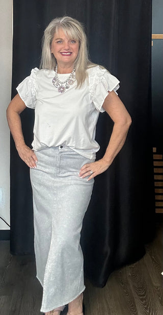 Woman wearing a white blouse with ruffled sleeves and a silver skirt against a black curtain.