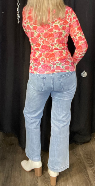 Person wearing a red floral top and blue jeans against a black curtain.