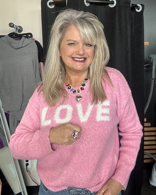 Woman wearing a pink sweater with 'LOVE' on it in a clothing store.