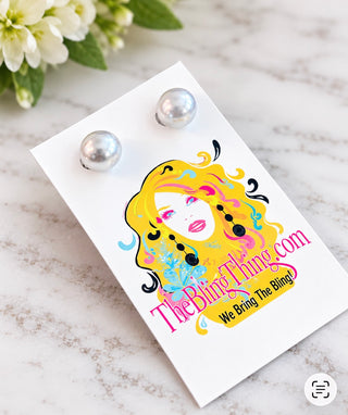 A pair of silver pearl stud earrings displayed on a white backing card featuring a colorful graphic of a woman with yellow hair and the text 'TheBlingThing.com We Bring The Bling!'.