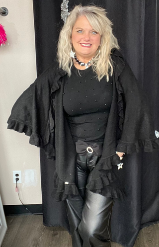 Person wearing a black outfit with ruffled details in front of a black curtain.