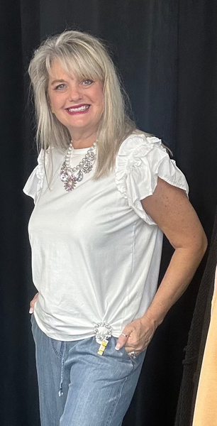 Woman wearing a white blouse and blue jeans standing next to a black backdrop with clothing on display.