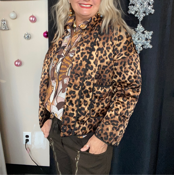 Woman wearing a leopard print jacket in a room with decorative items on the wall.