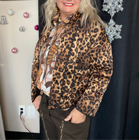 Woman wearing a leopard print jacket in a room with decorative items on the wall.