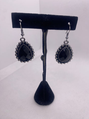 Black teardrop earrings on a black earring stand against a white background