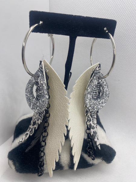 Pair of earrings with black and white feather-like designs on a black stand against a white background