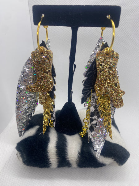 Feather-shaped earrings with gold, silver, and black colors on a black earring stand.