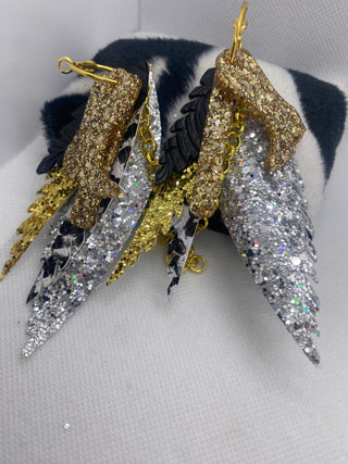Pair of glittery high-heeled shoe earrings on a white surface.