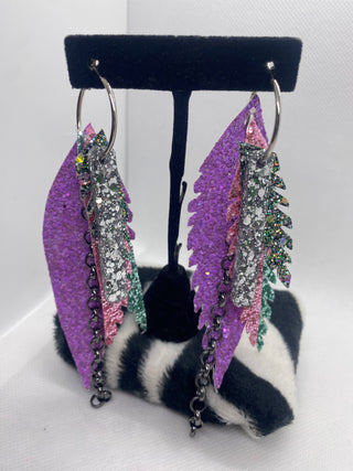 Purple feather-shaped earrings with decorative elements on a black and white striped surface.