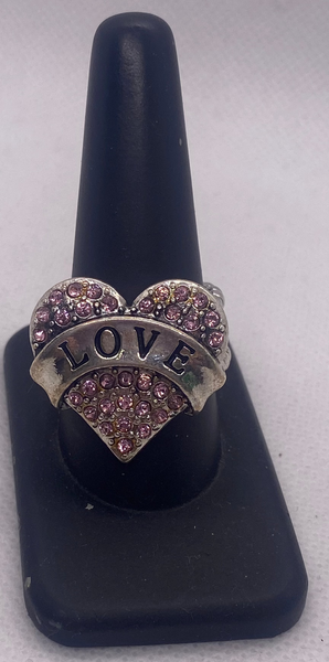 Heart-shaped ring with 'LOVE' engraving on a black stand against a gray background