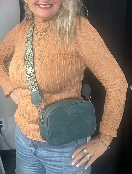 Woman wearing a mustard yellow sweater and blue jeans, holding a green crossbody bag.