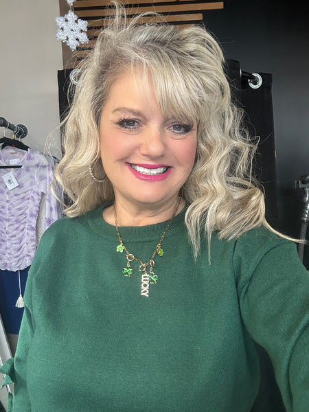 Woman wearing a green sweater with a necklace, standing in a store setting.