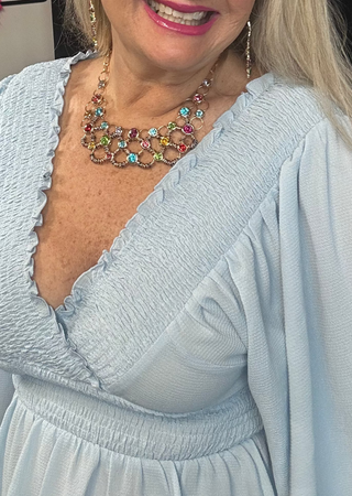 Woman wearing a light blue dress with a colorful necklace in an indoor setting.