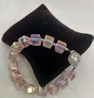 Bracelet with iridescent beads on a black cushion against a white background