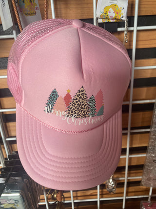 A pink trucker hat with leopard print accents and a Christmas tree graphic on the front, displayed on a rack.