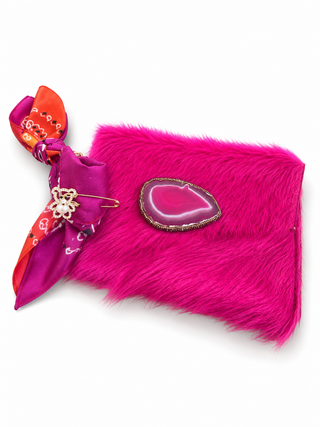 A hot pink faux fur clutch bag featuring a decorative teardrop-shaped agate slice inlay and a bright pink and orange patterned silk scarf tied to the side.