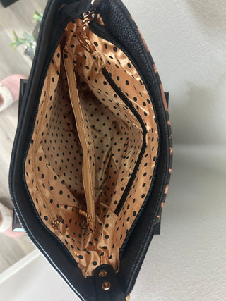 Close-up of the interior of a black handbag or clutch, showing a tan and black polka-dot lining with multiple zip compartments and gold-tone hardware.