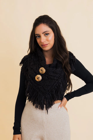 Woman wearing a black fringed vest over a black long-sleeve top on a beige background