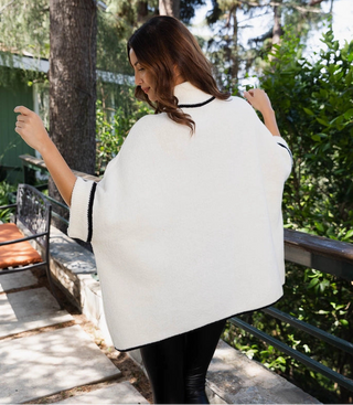Woman wearing a white cape with black trim outdoors