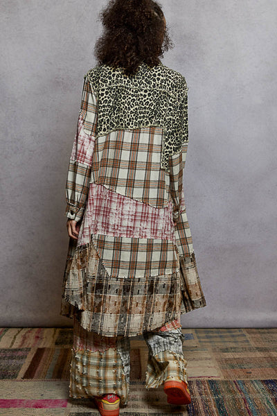 Person wearing a patterned outfit with a checkered dress and leopard print top, standing against a plain wall.