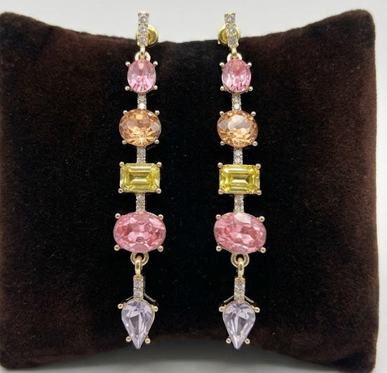 Pair of long earrings with multicolored gemstones on a brown cushion against a white background