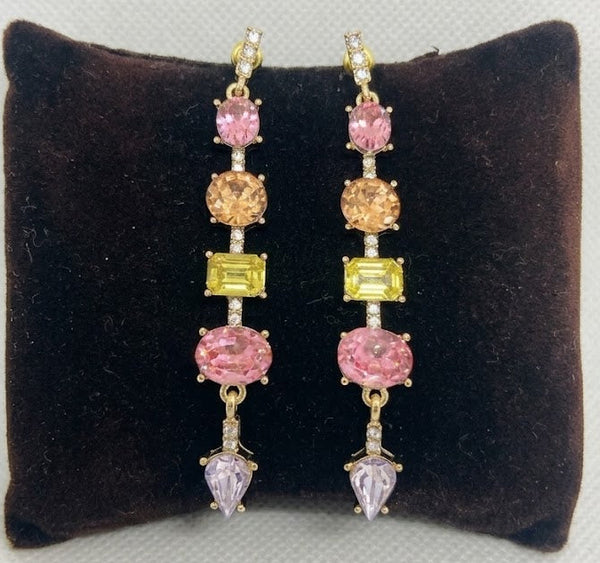 Pair of earrings with multicolored gemstones on a brown cushion against a light gray background