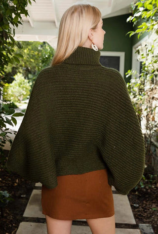 Person wearing a green poncho and brown skirt standing outdoors.