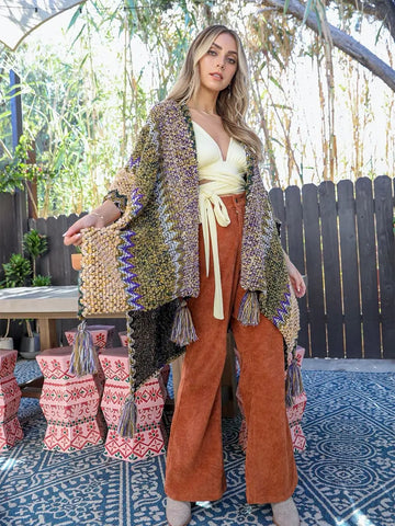 Woman wearing a patterned cardigan and orange pants standing outdoors on a patio.