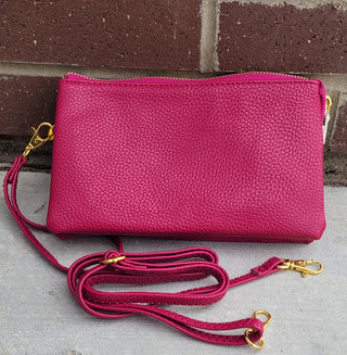 Pink leather clutch with a matching strap on a concrete surface with a brick wall background.